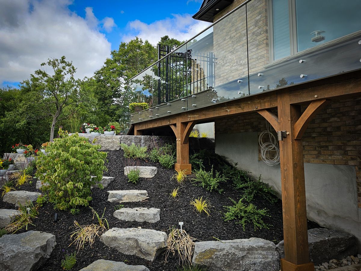  A house with a landscaped backyard featuring a timber-supported deck with glass railings and stone pathways.